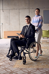 Image showing A businessman in a wheelchair and his female colleague together in a modern office, representing the power of teamwork, inclusion and support, fostering a dynamic and inclusive work environment.