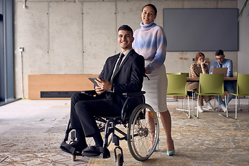 Image showing A businessman in a wheelchair and his female colleague together in a modern office, representing the power of teamwork, inclusion and support, fostering a dynamic and inclusive work environment.