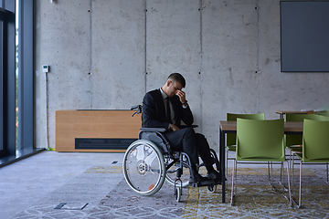 Image showing A melancholic businessman in a wheelchair sitting with a sad expression, gazing through the window of a modern office, conveying a sense of solitude