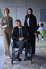 Image showing A businessman with disability in a wheelchair is surrounded by supportive colleagues in a modern office, showcasing the strength of teamwork, inclusivity, and empowerment in the face of challenges.