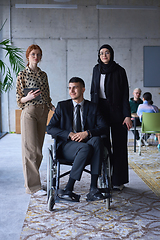 Image showing A businessman with disability in a wheelchair is surrounded by supportive colleagues in a modern office, showcasing the strength of teamwork, inclusivity, and empowerment in the face of challenges.