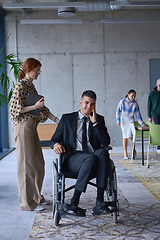 Image showing A businessman in a wheelchair and his female colleague together in a modern office, representing the power of teamwork, inclusion and support, fostering a dynamic and inclusive work environment.