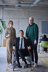 Image showing A businessman with disability in a wheelchair is surrounded by supportive colleagues in a modern office, showcasing the strength of teamwork, inclusivity, and empowerment in the face of challenges.