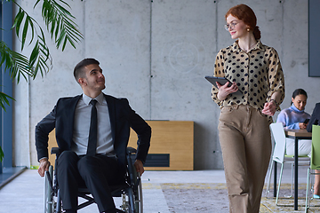 Image showing A businessman in a wheelchair and his female colleague together in a modern office, representing the power of teamwork, inclusion and support, fostering a dynamic and inclusive work environment.