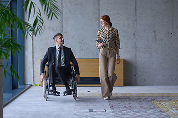 Image showing A businessman in a wheelchair and his female colleague together in a modern office, representing the power of teamwork, inclusion and support, fostering a dynamic and inclusive work environment.