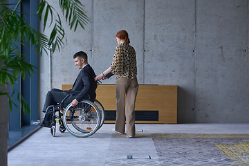 Image showing A businessman in a wheelchair and his female colleague together in a modern office, representing the power of teamwork, inclusion and support, fostering a dynamic and inclusive work environment.