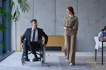 Image showing A businessman in a wheelchair and his female colleague together in a modern office, representing the power of teamwork, inclusion and support, fostering a dynamic and inclusive work environment.