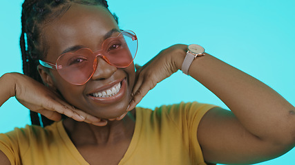 Image showing Happy, heart and portrait of a black woman with sunglasses for summer on a blue background. Smile, perfect and a model or African girl with trendy eyewear, fashion and hands on face on a backdrop