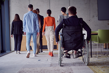 Image showing A diverse group of businessmen, including a businessman in wheelchair, confidently stride together through a modern, spacious office, epitomizing collaboration, inclusivity, and strength in unity
