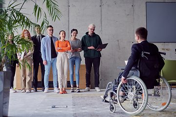 Image showing A group of diverse entrepreneurs gather in a modern office to discuss business ideas and strategies, while a colleague in a wheelchair joins them.