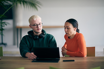 Image showing A young entrepreneurial couple sits together in a large, modern office, engaged in analyzing statistics and data on their laptop