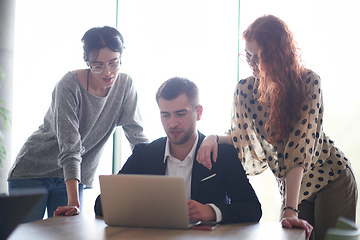 Image showing A businessman engaging in a discussion about sales statistics with his two female colleagues while they examine the data on a laptop in a modern office setting