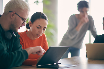 Image showing A young entrepreneurial couple sits together in a large, modern office, engaged in analyzing statistics and data on their laptop