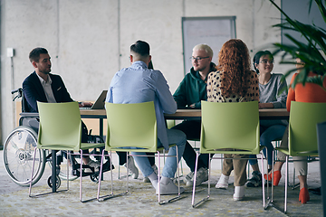 Image showing A diverse group of business professionals, including an person with a disability, gathered at a modern office for a productive and inclusive meeting.