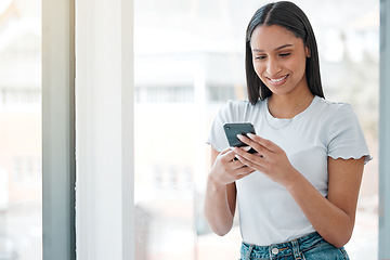 Image showing Whats everyone doing tonight. an attractive young woman standing alone at home and using her cellphone.