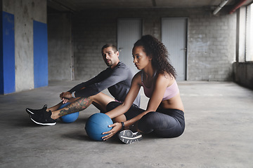 Image showing Lets get the ball rolling. Full length shot of sporty young couple sitting down and exercising with a ball inside a parking lot.