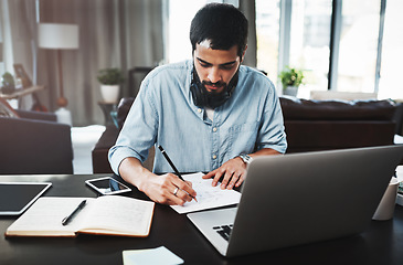 Image showing He mastered working from home effectively. a young man making notes while busy working from home.