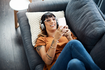 Image showing Music has a relaxing effect on our minds and bodies. a young woman wearing headphones while using her cellphone at home.