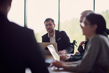 Image showing A diverse group of business professionals, including an person with a disability, gathered at a modern office for a productive and inclusive meeting.