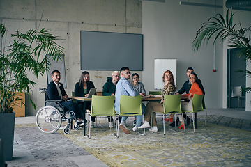 Image showing A diverse group of business professionals, including an person with a disability, gathered at a modern office for a productive and inclusive meeting.