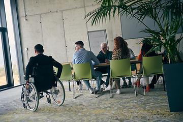 Image showing A diverse group of business professionals, including an person with a disability, gathered at a modern office for a productive and inclusive meeting.