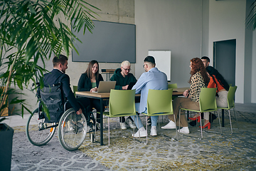 Image showing A diverse group of business professionals, including an person with a disability, gathered at a modern office for a productive and inclusive meeting.