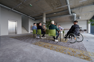 Image showing A diverse group of business professionals, including an person with a disability, gathered at a modern office for a productive and inclusive meeting.