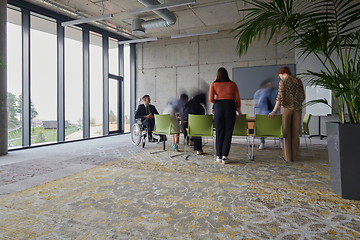 Image showing A businessman in a wheelchair sits at a table in a large, modern office, while his colleagues gather around, their steps blurred, symbolizing inclusivity, support, and unity in the face of challenges.