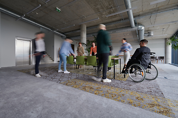 Image showing A businessman in a wheelchair sits at a table in a large, modern office, while his colleagues gather around, their steps blurred, symbolizing inclusivity, support, and unity in the face of challenges.