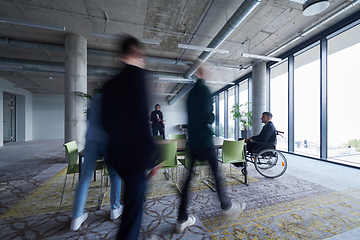 Image showing A businessman in a wheelchair sits at a table in a large, modern office, while his colleagues gather around, their steps blurred, symbolizing inclusivity, support, and unity in the face of challenges.