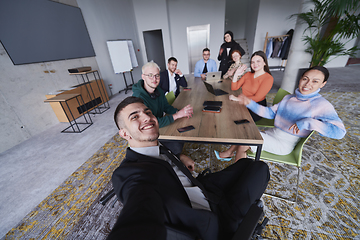 Image showing In a modern office, a group of businessmen gathers around a table during a meeting, capturing a moment of camaraderie and teamwork as they take a selfie