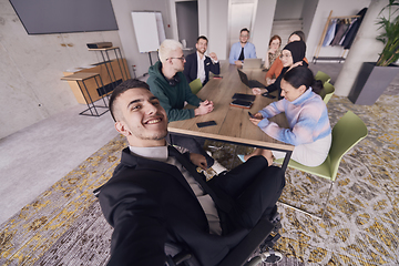 Image showing In a modern office, a group of businessmen gathers around a table during a meeting, capturing a moment of camaraderie and teamwork as they take a selfie