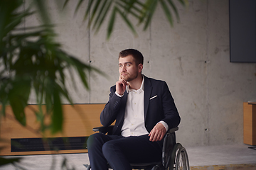 Image showing A melancholic businessman in a wheelchair sitting with a sad expression, gazing through the window of a modern office, conveying a sense of solitude