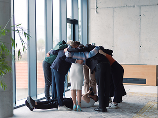 Image showing Offstage. The photographer takes a photo of a diverse group of businessmen in a modern office who hug each other in a circle