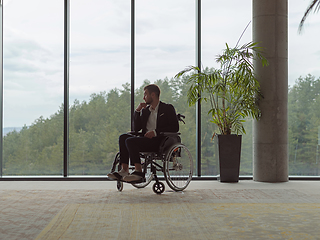 Image showing A melancholic businessman in a wheelchair sitting with a sad expression, gazing through the window of a modern office, conveying a sense of solitude