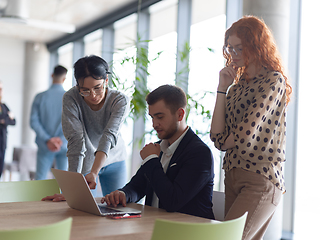 Image showing A businessman engaging in a discussion about sales statistics with his two female colleagues while they examine the data on a laptop in a modern office setting