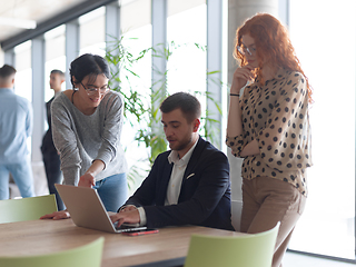 Image showing A businessman engaging in a discussion about sales statistics with his two female colleagues while they examine the data on a laptop in a modern office setting