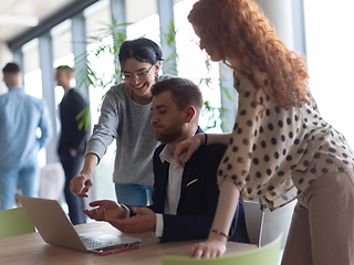 Image showing A businessman engaging in a discussion about sales statistics with his two female colleagues while they examine the data on a laptop in a modern office setting