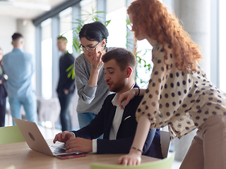 Image showing A businessman engaging in a discussion about sales statistics with his two female colleagues while they examine the data on a laptop in a modern office setting