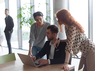 Image showing A businessman engaging in a discussion about sales statistics with his two female colleagues while they examine the data on a laptop in a modern office setting