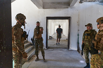 Image showing Group of soldiers discusses military tactics while situated in an abandoned building, meticulously planning their moves with focus and determination.