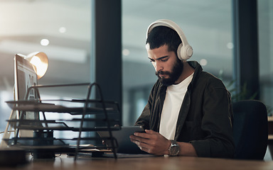 Image showing Load up your playlist, its gonna be a long night. a young businessman using a digital tablet with headphones during a late night at work.