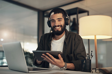 Image showing All set for a night of success. a young businessman using a digital tablet, laptop and headphones during a late night at work.