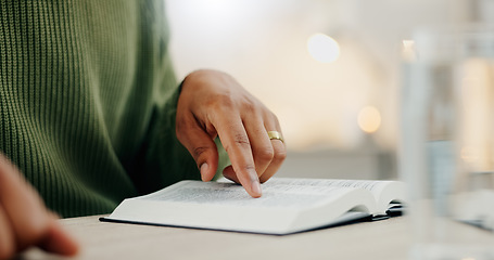 Image showing Closeup hand, reading and a bible for faith, spiritual support or hope from scripture. House, table and a person with a book for worship, trust or education on God, Jesus or learning about religion