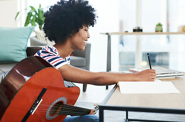 Image showing I enjoy making my own music. a woman writing in her notebook while playing the guitar at home.