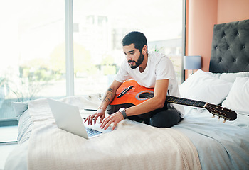 Image showing Learning how to play the guitar from home. a man using his laptop while playing the guitar at home.