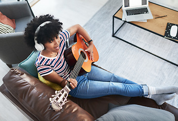 Image showing Playing the guitar makes me feel good. a woman wearing headphones while playing the guitar at home.