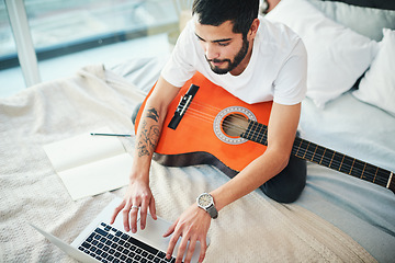 Image showing Im taking virtual lessons to learn more about playing the guitar. a man using his laptop while playing the guitar at home.