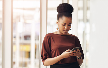 Image showing Shes staying connected. an attractive young businesswoman using her cellphone while standing in the office.