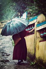 Image showing Buddhist monk with umbrella spinning prayer wheels